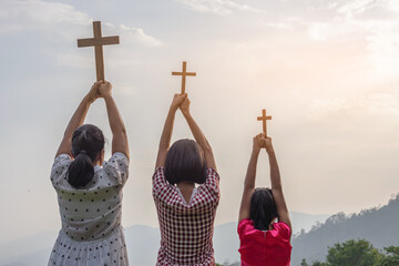 Children praying to the GOD while holding a crucifix symbol with bright sunbeam on the mountain