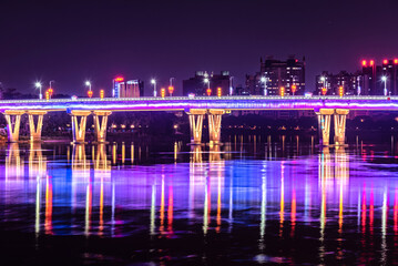 Fototapeta na wymiar Night view of city bridge. Colorful lights reflected on the water. Cityscape in DongGuang, Guangdong, China.