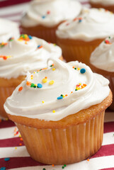 Vanilla cupcakes with sprinkles on a red and white tablecloth.