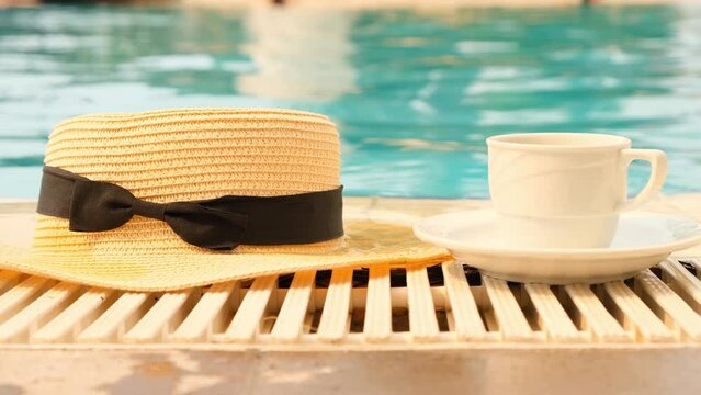 cup of coffee and a straw hat on the background of a swimming pool on a summer sunny day. Good morning concept and planning a new day, week, month. Vacation and travel.