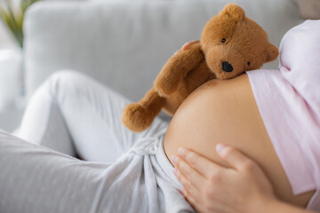 Pregnant woman caressing belly hugging teddy bear baby toy on pregnancy bump waiting for the birth of her child