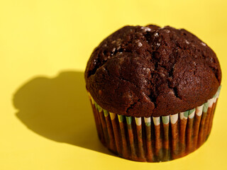 One homemade freshly baked delicious chocolate muffin served on bright trend yellow paper background with hard shadows, closeup, side view. Fresh handmade pastry. DIY. Copy space for text