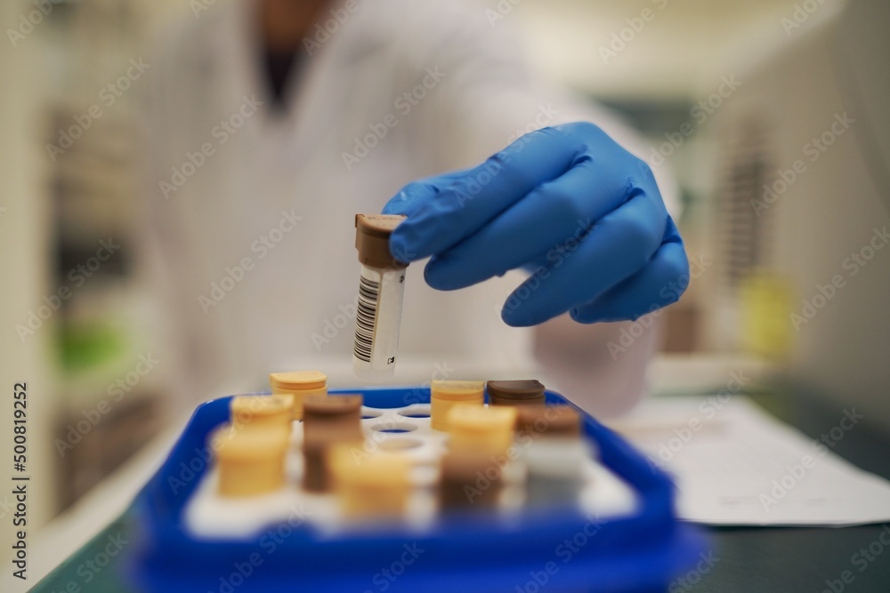 Poster a gloved hand picking up a sample vial from a tray in a laboratory environment.