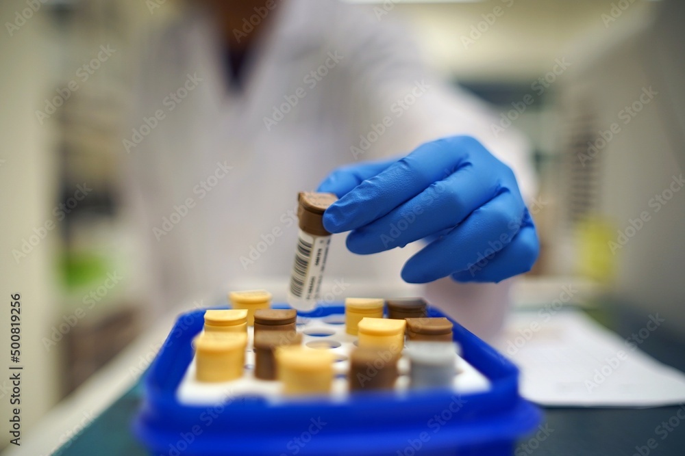Poster a gloved hand handling a sample vial from a tray in a laboratory setting.