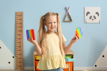 Happy little girl holding different pop it fidget toys in child room