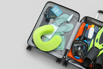 Suitcase with beach accessories, snorkeling mask and immune passport on light background