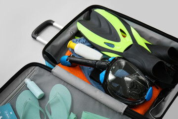Suitcase with beach accessories and snorkeling mask on light background