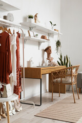 Comfortable workplace and rack with clothes near light wall in stylish room interior