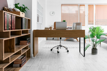 Interior of light office with modern workplace, shelving units and stylish clock on light wall