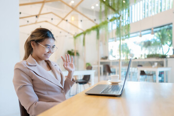Obraz premium Asian business woman happy smile wear glasses and working on computer laptop in cafe. She meeting video call. New normal, Covid-19 and pandemic concept