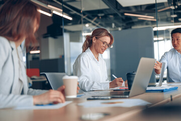 view of smiling multiethnic businesspeople in formal wear at table during conference in office.