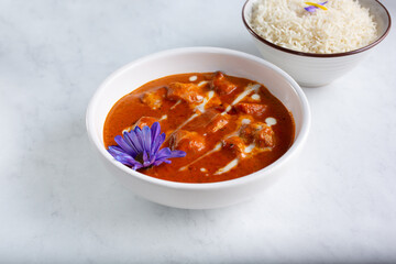 A view of a bowl of butter chicken, with a bowl of basmati rice.