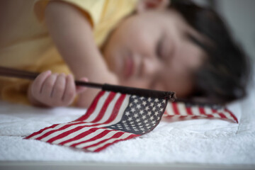 Baby child sleeping in bed holding American flag in hand, 4 th July,  Independence day, Flag day concept, selective focus