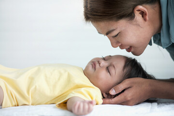 Side view portrait of Asian mother kissing her baby daughter sleeping on a bed, Mother's day concept