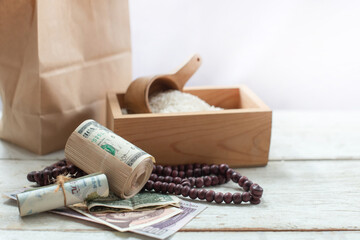 Fototapeta na wymiar Banknote, rosary, brown paper bag and rice in the wooden box, ZAKAT donation for Muslims according to religious principles during the Ramadan month