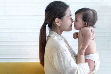 Young mother plays with her little baby daughter by raising both hands, rubbing nose to nose with close eyes