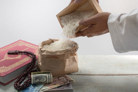 Muslim's hand pouring the rice into brown paper bag over white background, Quran holy book banknote, rosary on table, ZAKAT donation, Muslim tradition concept