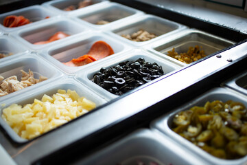 A view of a station full of pizza toppings and ingredients, seen at a local pizzeria.