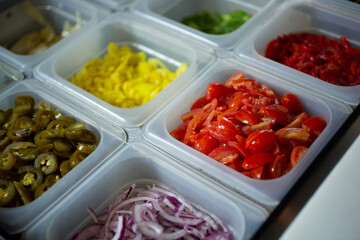A view of a station full of pizza toppings and ingredients, seen at a local pizzeria.