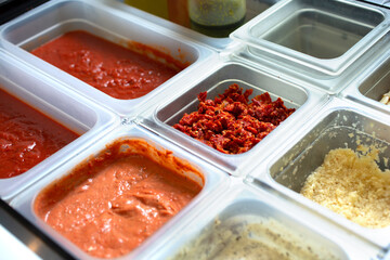 A view of a station full of pizza toppings and ingredients, seen at a local pizzeria.