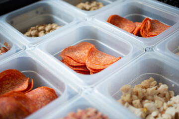 A view of a station full of pizza toppings and ingredients, seen at a local pizzeria.