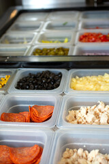 A view of a station full of pizza toppings and ingredients, seen at a local pizzeria.