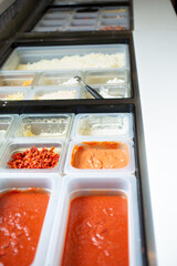 A view of a station full of pizza toppings and ingredients, seen at a local pizzeria.