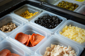 A view of a station full of pizza toppings and ingredients, seen at a local pizzeria.