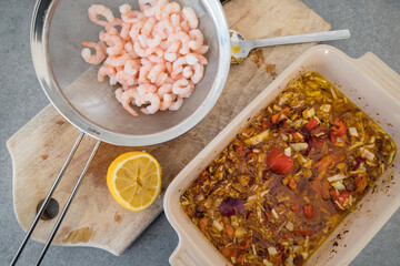 Rinsed small shrimp in a colander on a board with lemon and a pan with vegetables to grill.