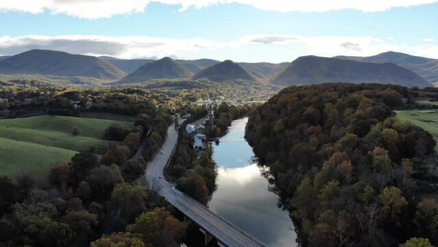 Aerial footage above a river and entering a small town in the Appalachian mountains.  River is still and reflection of the sky can be seen.  A four lane bridge crosses the river.