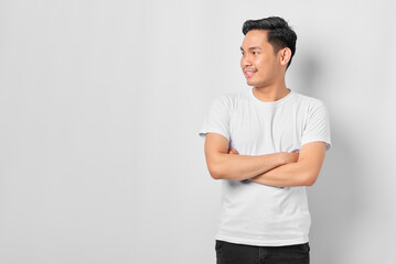 Portrait of smiling young Asian man crossed arms and looking aside at blank space isolated on white...