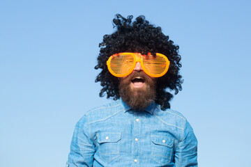 Crazy funny bearded man with wig and fun glasses on sky background. Funny bearded man in wig....