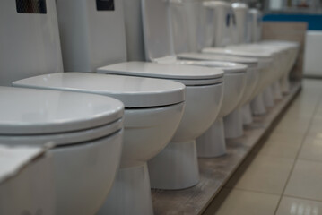 Plumbing, white toilets standing in a row in a store. Close-up, selective focus, side view