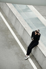 Female jogger resting after training and listening to music in headphones