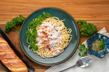 Spaghetti carbonara with Ham and  Bacon on green plate on wooden table.