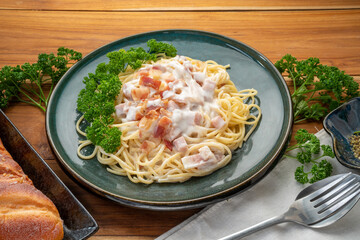 Spaghetti carbonara with Ham and  Bacon on green plate on wooden table.