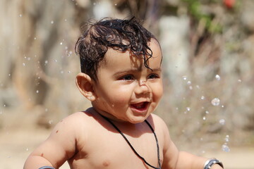 Photo of A small cute Indian Hindu baby child expresses happiness while taking a water bath with unclothed