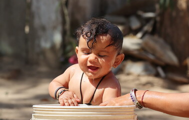 Photo of A small newborn indian baby taking a bath with a bucket full of water with unclothed