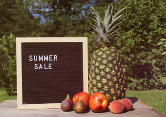 Fresh Pineapple outdoors with Apricots, Peaches and figs. sale sign garden in background