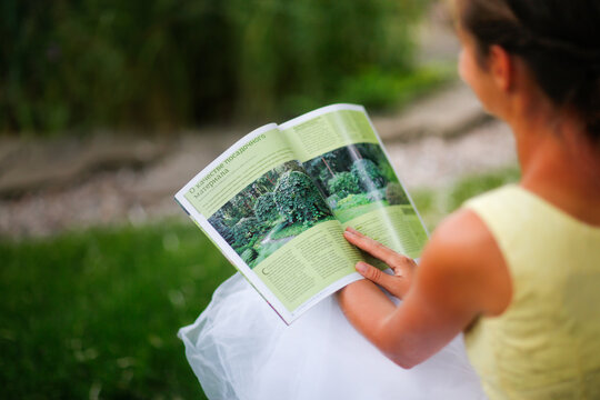 Cute european girl woman looking at gardening magazine in beautiful garden, landscaping art and well maintained garden