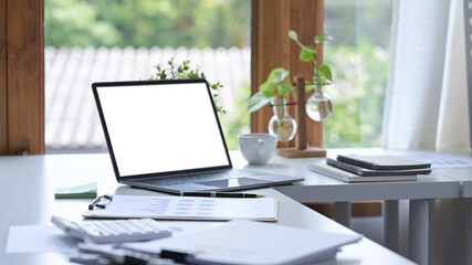 Fototapeta premium Comfortable workplace with computer laptop, documents, coffee cup and houseplant on white table.