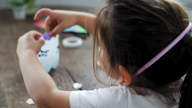 Caucasian preschool girl doing crafts with plastic bottle and paints. Recycle upcycling waste. Sustainable lifestyle