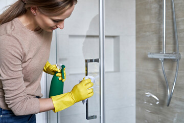 Young caucasian woman cleaning shower glass