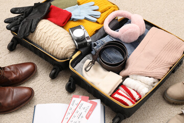 Open suitcase with warm clothes, accessories and shoes on floor