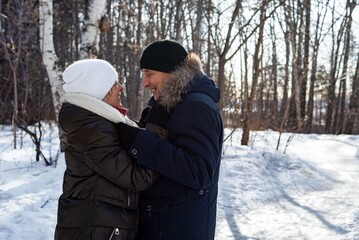 Fototapeta na wymiar Elderly couple hugging each other and looking at each other in the countryside at sunset in the winter forest, family relationship. Life style