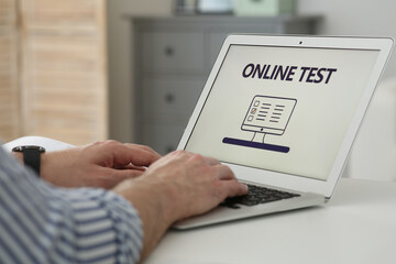 Man taking online test on laptop at desk indoors, closeup