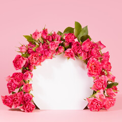 Fresh tiny pink roses as framing of white circle arch niche or podium on soft light pink stage mockup for presentation cosmetic products, goods, advertising, design, card, poster, square, closeup.