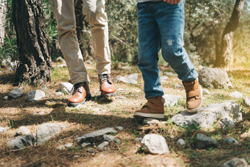 Close-up view of tourists school boy and his dad feet boots walking a stone footpath in spring...