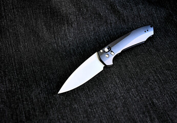 Folding knife silver cutting stainless edge black handle denim macro background
