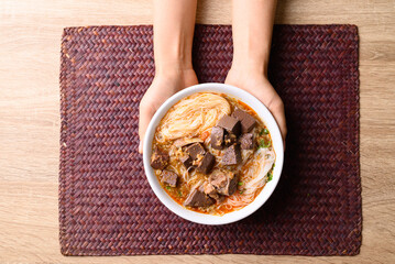 Northern Thai food, Spicy rice noodles soup with pork in bowl holding by hand, Local Thai food, Table top view